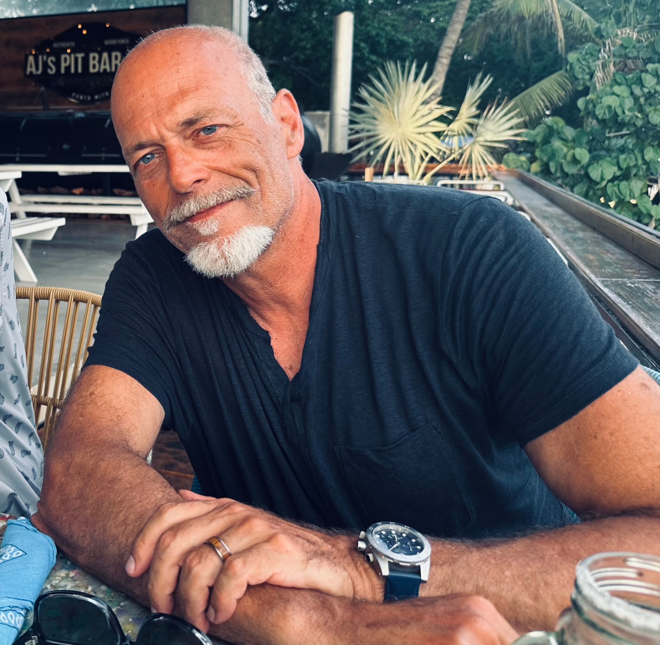 light skinned man sitting at a table with arms lightly folded