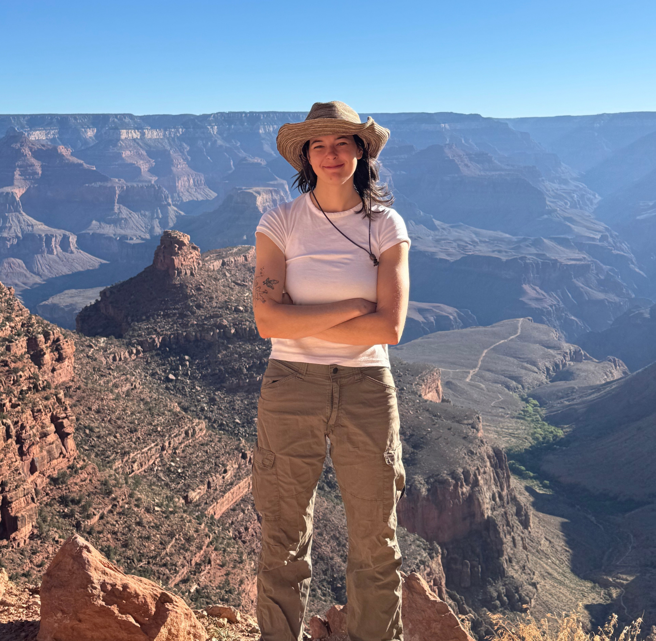 Hannah Gray_Staff Webpg headshot Light skinned woman standing with her arms crossed with the Grand Canyon in the background